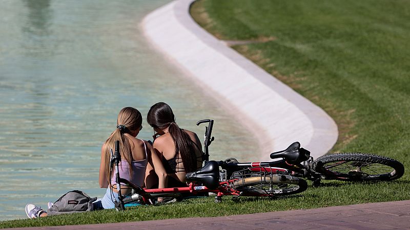 Dos jóvenes descansan junto a un estanque en Valencia.