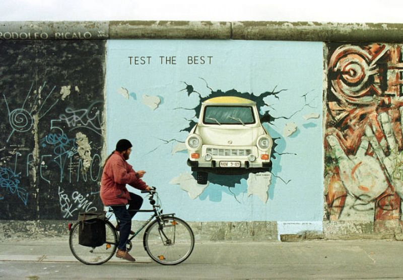 Un ciclista pasa ante una de las más famosas pintadas del Muro de Berlín, en la que un Trabant, un coche de la RDA, rompiendo el muro.