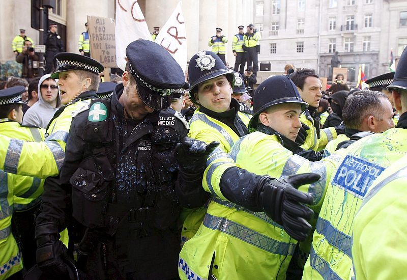 Varios agentes de policía se protegen de la pintura que les tira un grupo de activistas