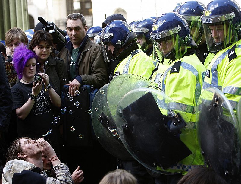 Un antisistema hace pompas de jabón sentado frente a la policía en la City de Londres.