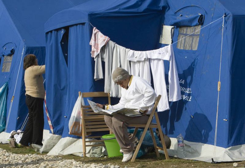Un hombre lee el periódico junto a una tienda de campaña del campo de desplazados de L'Aquila.