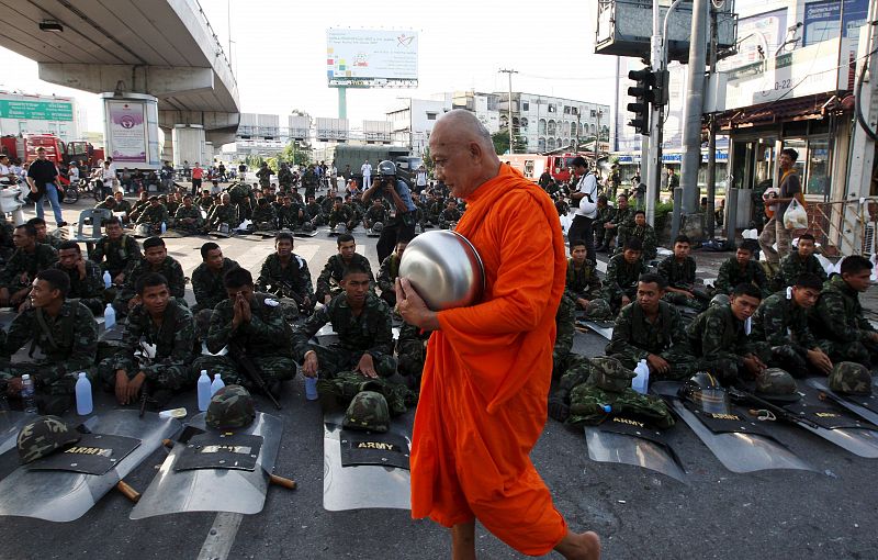 Un monje cruza una calle de Bangkok en la que descansan decenas de soldados tailandeses.