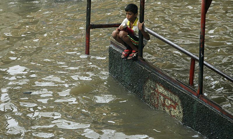 A boy sits at a flooded bus-stop after heavy rains in Mumbai