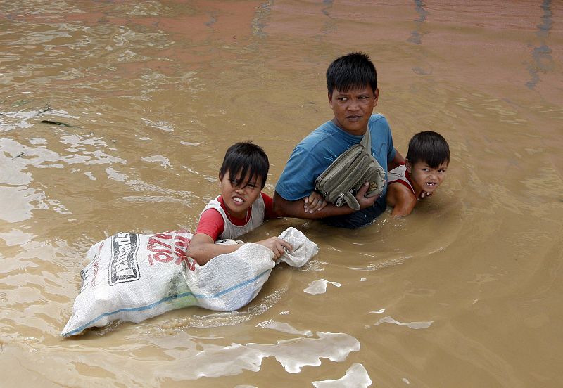 Un padre ayuda a sus hijos a cruzar una calle completamente inundada, en la población de Santa Cruz, en la provincia de Laguna, al sur de Manila (Filipinas),