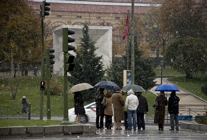 Varias personas se protegen de la nieve en un paso de peatones de la madrileña Plaza de San Juan de la Cruz.