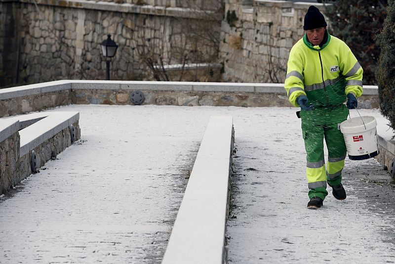 Un operario esparce sal por las calles de Ávila para derretir la nieve que ha caído sobre la ciudad.