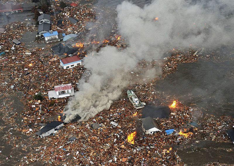 Houses swept by a tsunami smoulder near Sendai Airport in Japan