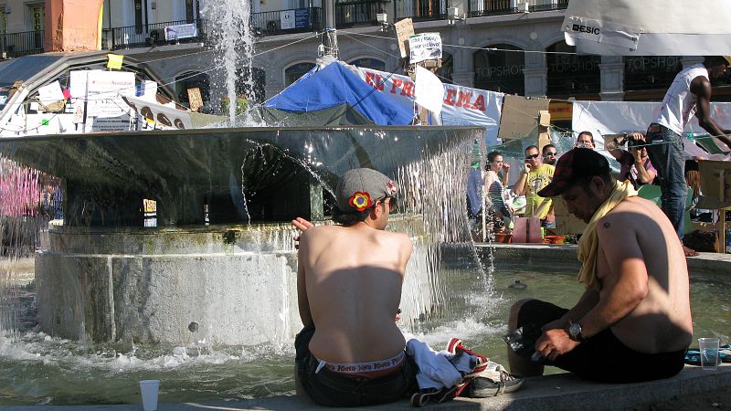 Los acampados se refrescan como pueden en las fuentes de la Puerta del Sol.