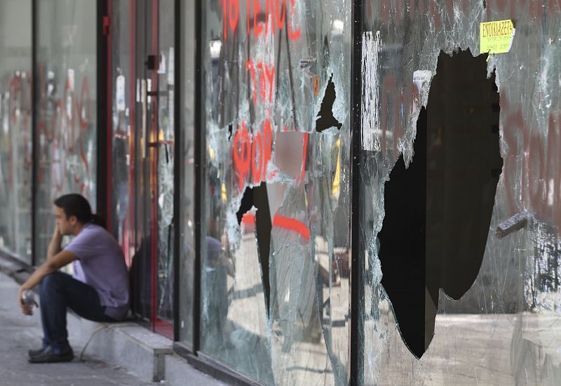Un hombre habla por teléfono junto a un escaparate destrozado tras dos días de violentos enfrentamientos en la plaza Syntagma en Atenas.