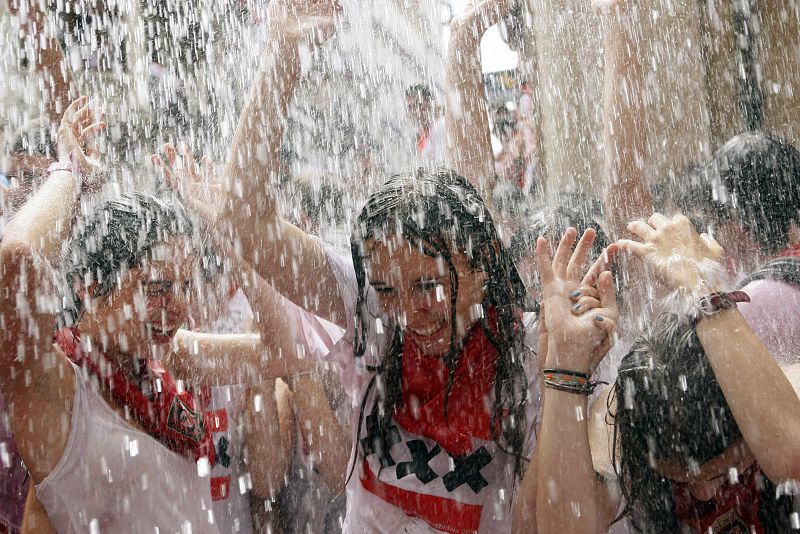 Los asistentes al chupinazo se mojan con el agua que les arrojan desde los balcones