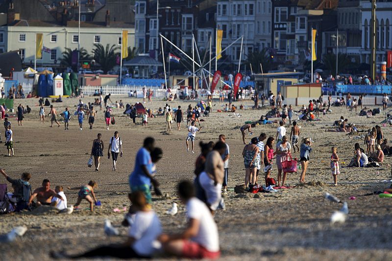 Numerosas personas disfrutan del buen clima, en la bahía de Weymouth, donde cientos de regatistas se entrenan de cara al comienzo de los Juegos Olímpicos de Londres 2012.
