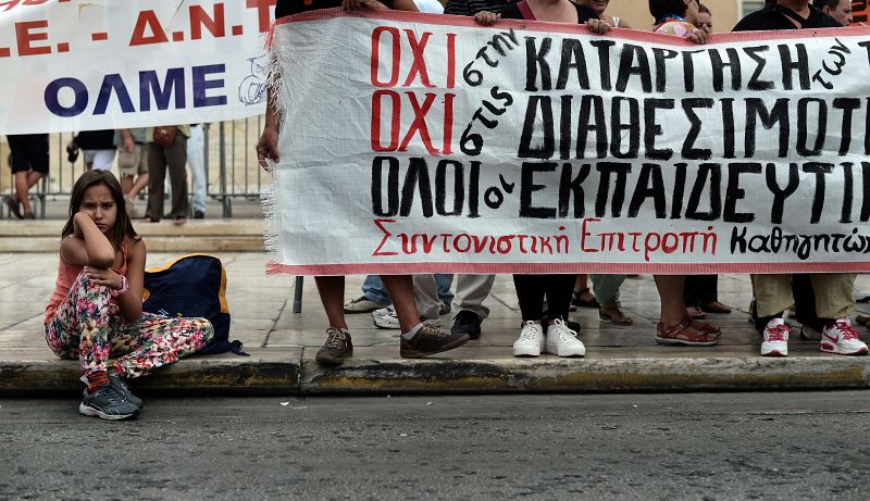 Una niña sentada en la acera mientras el personal de los colegios se manifiesta frente al Parlamento griego en Atenas