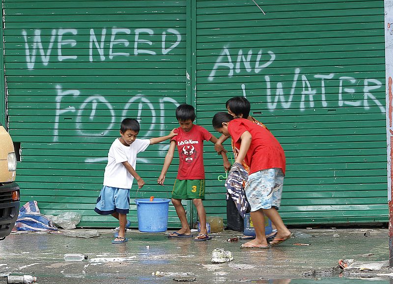 Niños en Tacloban frente a una pintada en la que se puede leer "Necesitamos comida y agua"