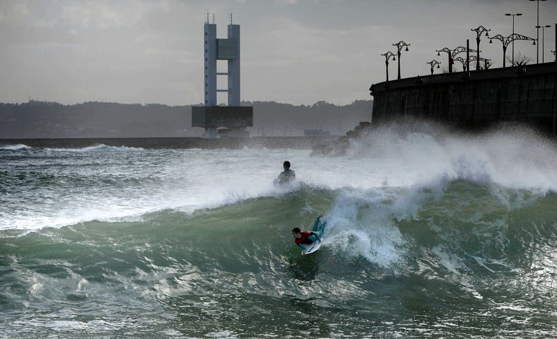 Varios jóvenes practicaron este lunes surf esta mañana en la playa de San Amaro de A Coruña, en una jornada marcada por la alerta roja en todo el litoral gallego.