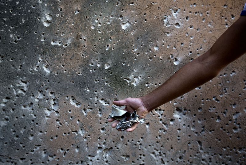 Un hombre palestino muestra la metralla frente a un muro con impactos tras el ataque israelí en Beit Hanun, al norte de la franja de Gaza.