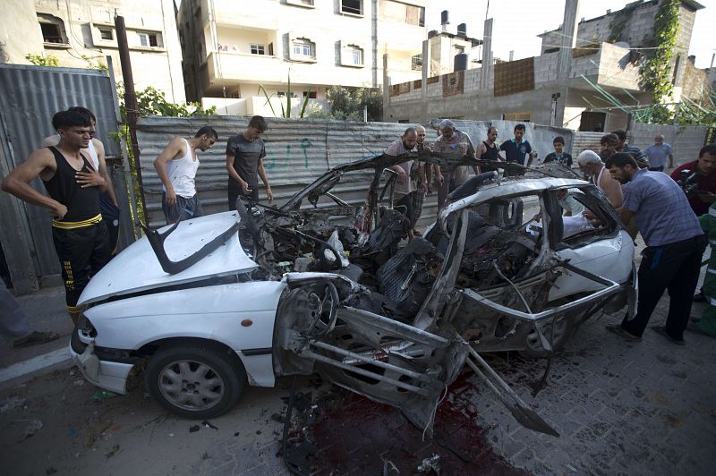 Un grupo de palestinos inspecciona un coche destrozado durante la ofensiva israelí en la Franja de Gaza 
