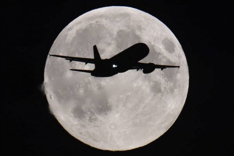 Un avión de pasajeros desciende hacia el aeropuerto londinense de Heathrow con la luna llena al fondo.