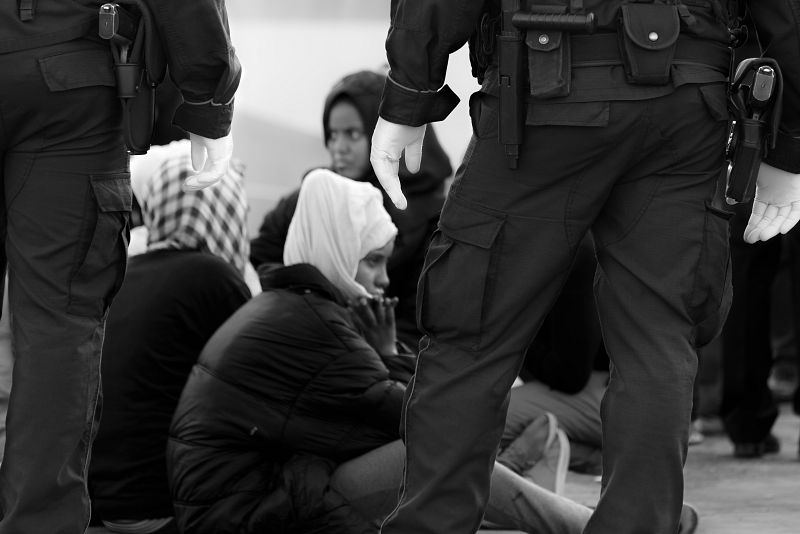 Mujeres recién llegadas a Lampedusa, sentadas en el suelo bajo la atenta mirada de la autoridad.