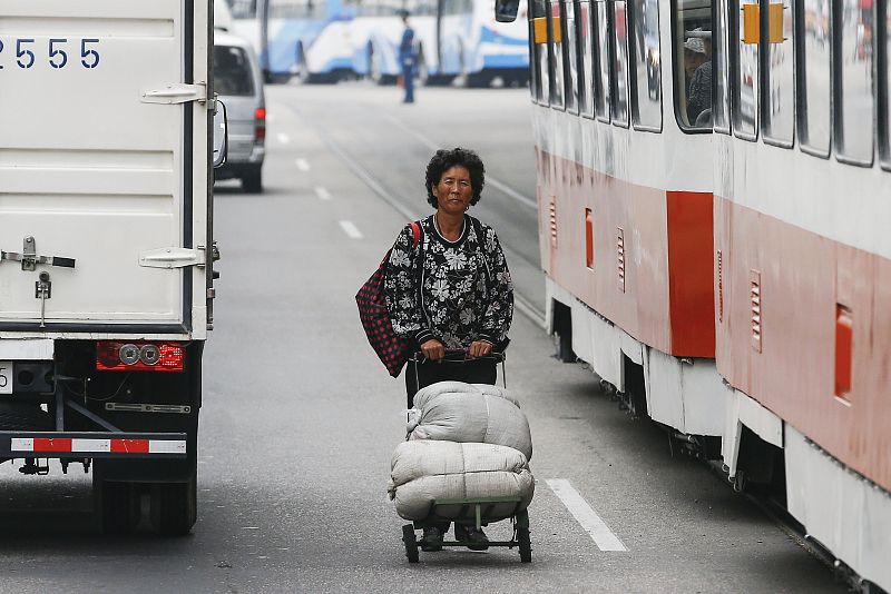 Una mujer empuja un carrito entre los coches en el centro de Pyongyang