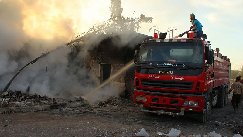 Un miembro de la Defensa Civil y un vecino extinguen un fuego después del ataque en Urm al-Kubra, cerca de Alepo