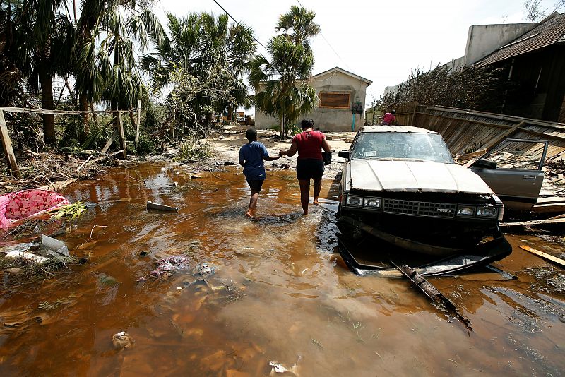 Una mujer y un niño caminan de la mano cerca de una casa dañada por el huracán Matthew en South Beach, Bahamas