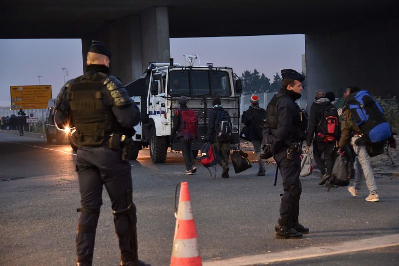 Policías franceses observan a los migrantes marcharse del campamento conocido como "La Jungla" en Calais