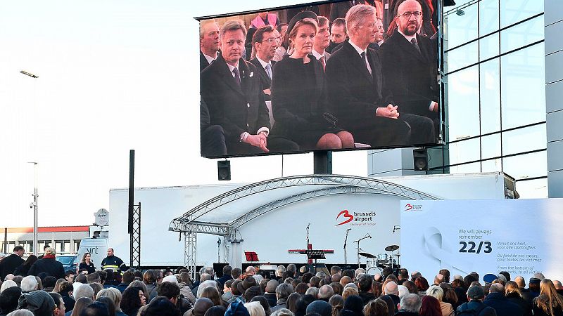 Los reyes de los belgas, Matilde y Felipe, y el primer ministro Charles Michel, en la pantalla durante la ceremonia de recuerdo a las víctimas de los atentados de Bruselas en el aeropuerto de Zaventem