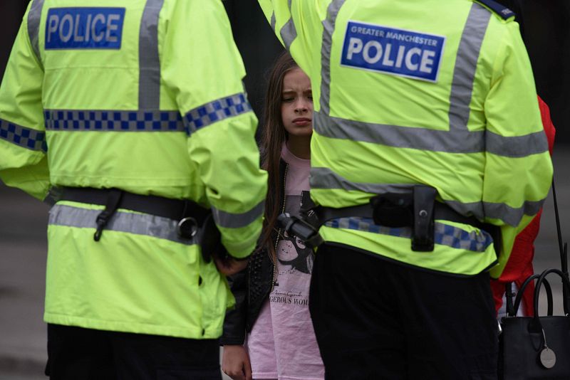 Una mujer y una niña ataviada con una camiseta de Ariana Grande hablan con dos agentes de policía en las inmediaciones del Manchester Arena