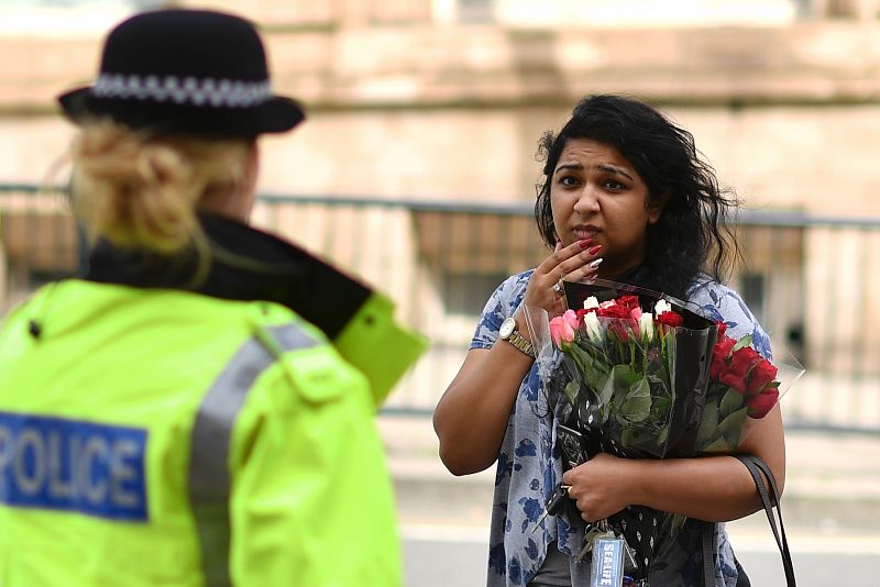 Una mujer con un ramo de flores habla con una agente de policía en las inmediaciones del Manchester Arena