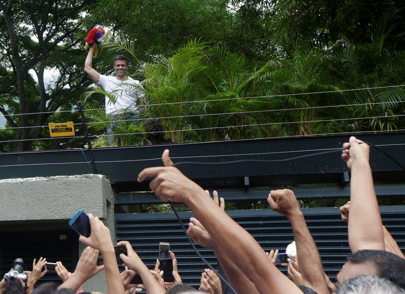El líder opositor venezolano saluda a sus simpatizantes desde la valla de su casa, en la que permanece en arresto domiciliario