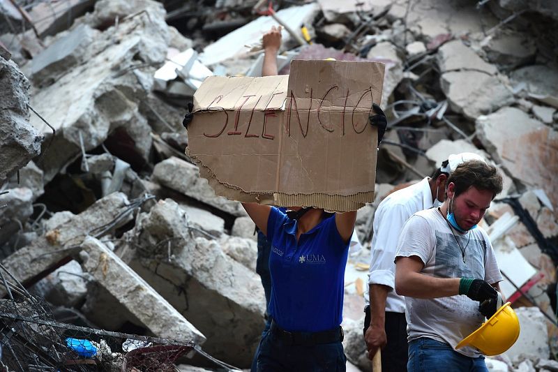 Un miembro de los equipos de rescate pide silencio para oir a los posibles supervivientes atrapados entre los escombros.