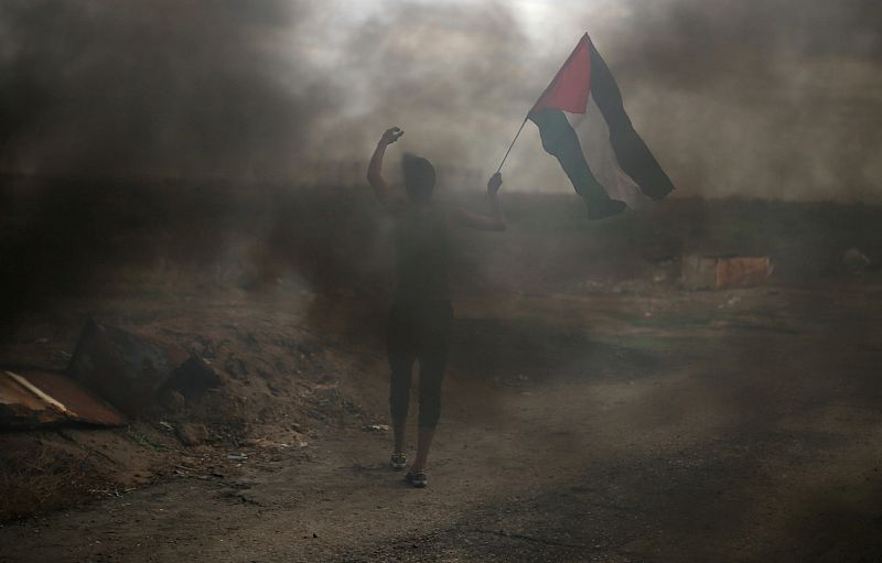 Un palestino sujeta una bandera durante los enfrentamientos con tropas israelíes cerca de la frontera de Gaza con Israel