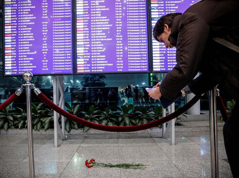 Un hombre toma una fotografía con su teléfono móvil de unas flores en el aeropuerto de Domodédovo en recuerdo de las víctimas del accidente