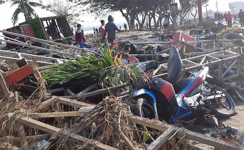La gente camina cerca de una tienda en la playa destruida por el tsunami que ha golpeado Palu