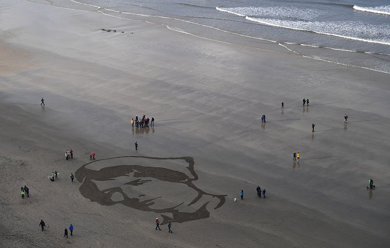 Gente observando el retrato de la enfermera militar Rachel Ferguson, que murió en junio de 1918, en la playa de Downhill en Coleraine, creada como parte del proyecto de Danny Boyle The Sea celebrations