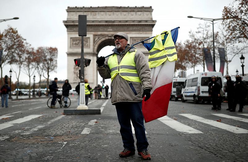 Un hombre con un chaleco amarillo y una bandera de Francia permanece frente al Arco del Triunfo