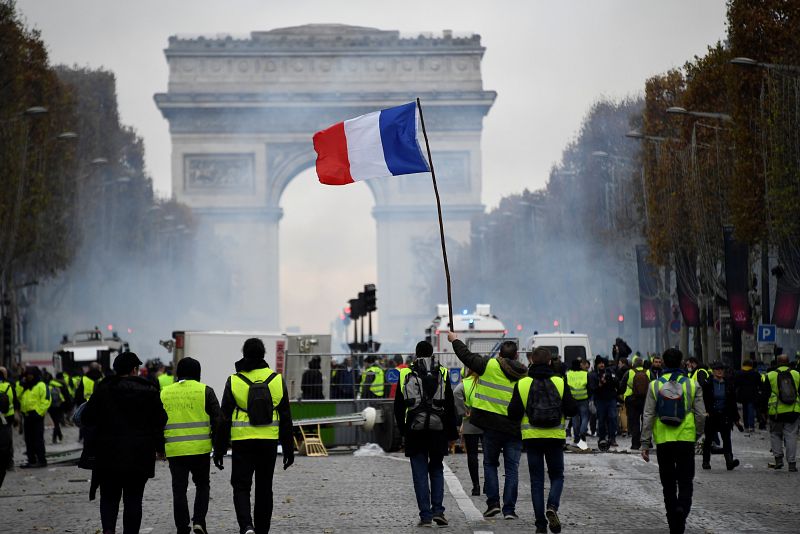 Un grupo de "chalecos amarillos" avanza por los Campos Elíseos ondeando una bandera de Francia