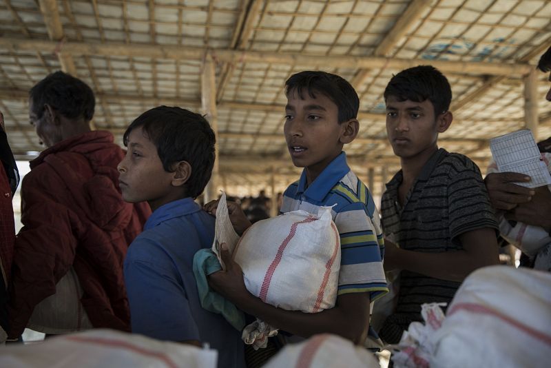 Niños y jóvenes refugiados hacen cola en un punto de distribución de ayuda en Nayapara; reciben arroz, aceite, sal, azúcar y bienes de primera necesidad, como ropa.