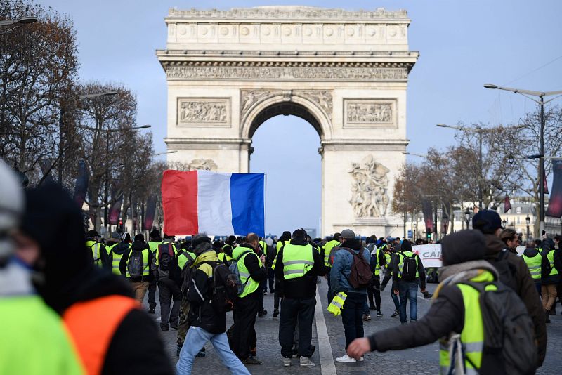 Los 'chalecos amarillos' portan una bandera de Francia en las inmediaciones del Arco del Triunfo