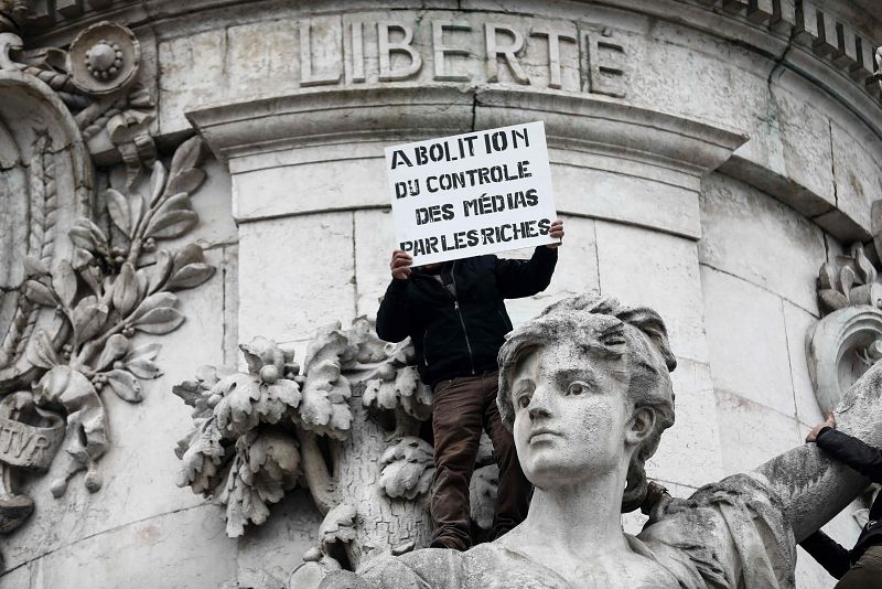 Un manifestante subido a la estatua de la República en la plaza homónima sostiene una pancarta en la que se puede leer "Abolición de los medios controlados por los ricos"