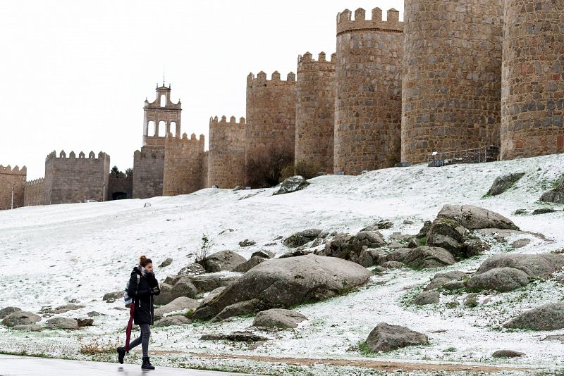 Una mujer camina junto al lienzo norte de la muralla de Ávila cubierta por una fina capa nieve caída en las últimas horas. 