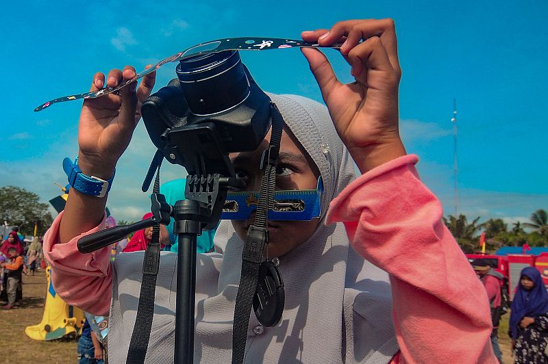Una niña coloca un filtro frente a su cámara mientras toma fotos de la Luna moviéndose frente al sol, en Siak, provincia de Riau, en Indonesia.