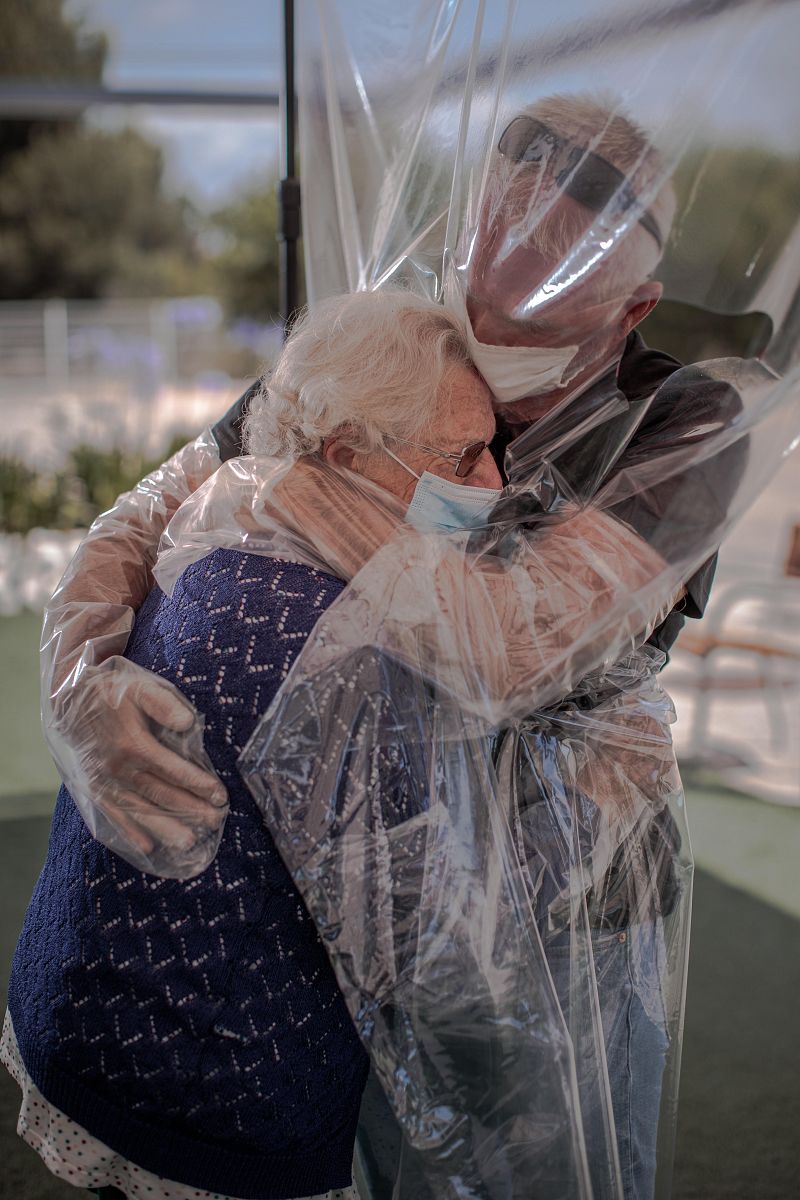 Una interna en una residencia de mayores abraza a su hijo a través de un plástico habilitado.
