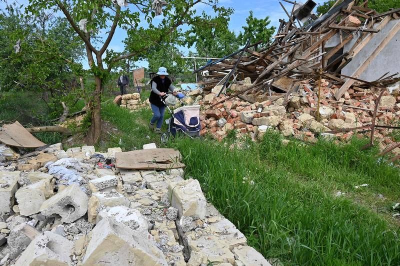 Una mujer lleva un cochecito con sus pertenencias mientras pasa por delante de una casa destruida en el pueblo de Vilkhivka, cerca de Járkov.