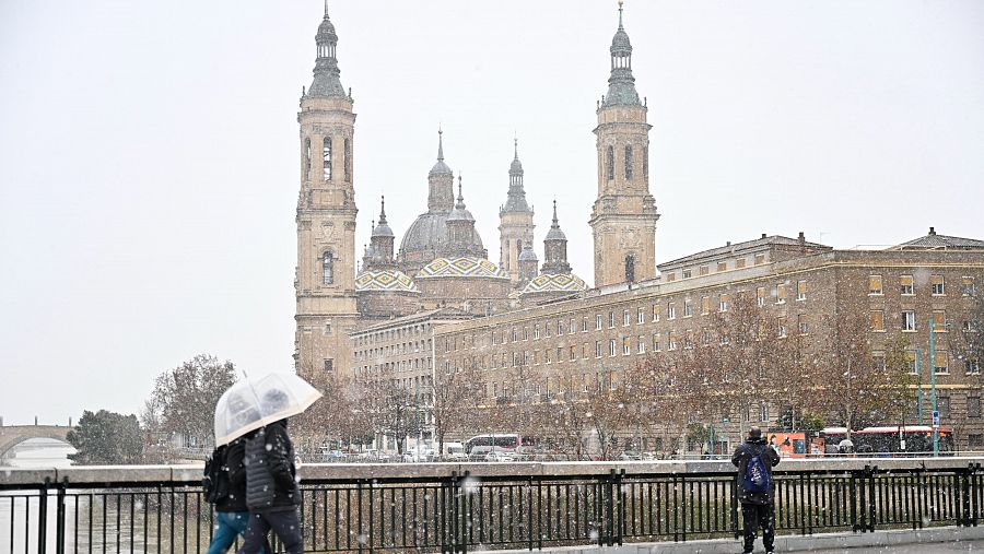 Varias personas caminan por la calle bajo la nieve en Zaragoza