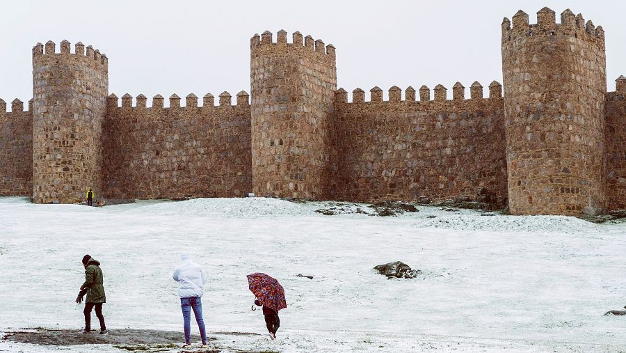 Tres personas caminan bajo la nieve en el lienzo norte de la muralla de Ávila