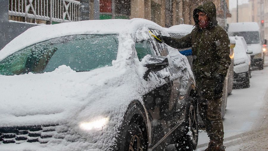 Un hombre retira la nieve de un vehículo drante la nevada de este viernes en Soria