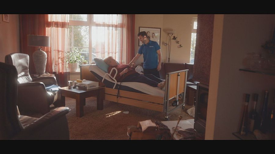 Anciana en uan camillay su cuidador al lado en el salón de una casa