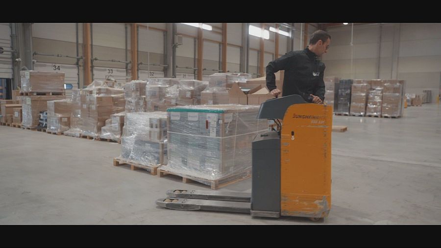 Hombre subido en una máquinas se desplaza por una nave llena de paquetes