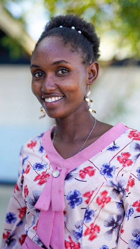 Retrato de mujer africana sonriendo con el pelo recogido y una camisa blanca con flores rojas y azules.